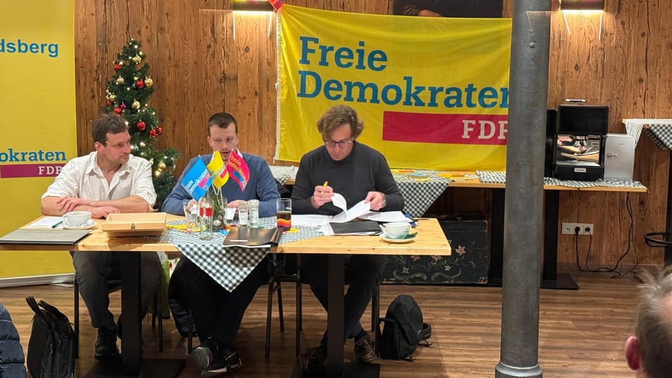 Das dreiköpfige Präsidium der Versammlung an einem Tisch mit FDP-Tischfähnchen vor dem Banner der Freien Demokraten, daneben ein geschmückter Weihnachtsbaum