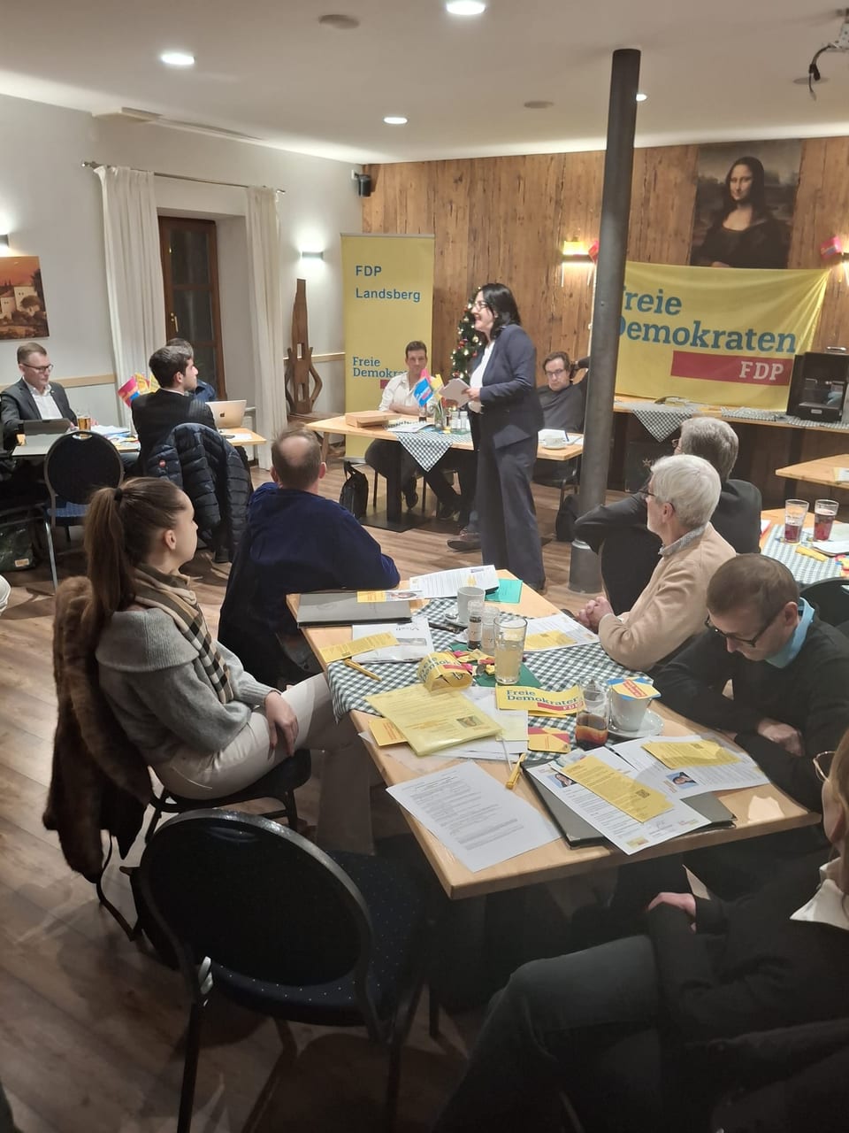 Spitzenkandidatin Ulla Schäfer spricht stehend zu den sitzenden Mitgliedern der Versammlung, im Hintergrund ein Rollup FDP Landsberg und das Banner der Freien Demokraten