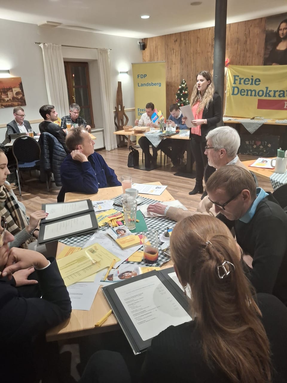 Angela Rehekampff spricht stehend zur Versammlung, im Hintergrund ein Rollup FDP Landsberg und das Banner der Freien Demokraten