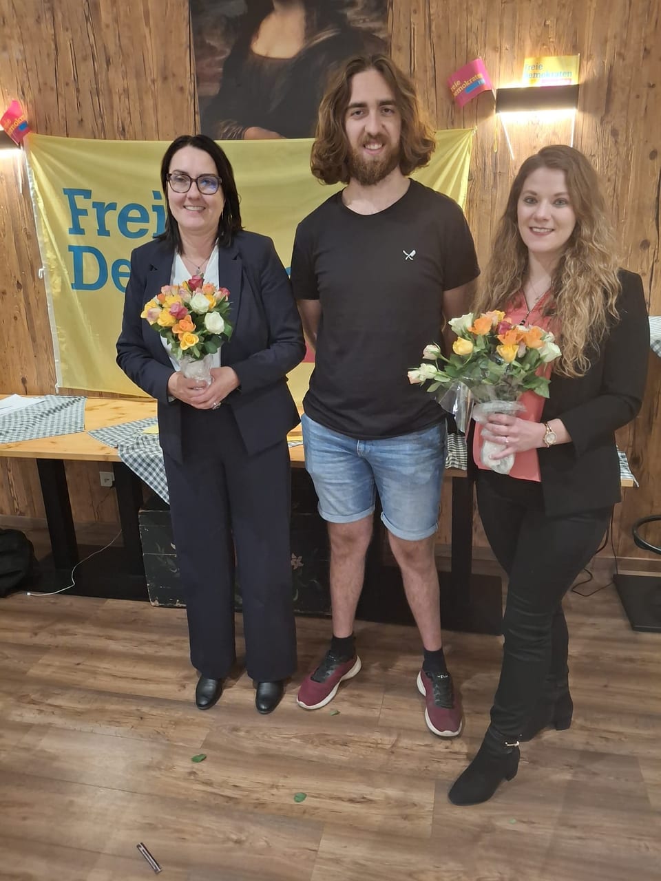 Die beiden Spitzenkandidatinnen Ulla Schäfer (links) und Angela Rehekampff (rechts) mit Blumensträußen, dazwischen ein weiterer Kandidat, vor dem gelben Banner der Freien Demokraten