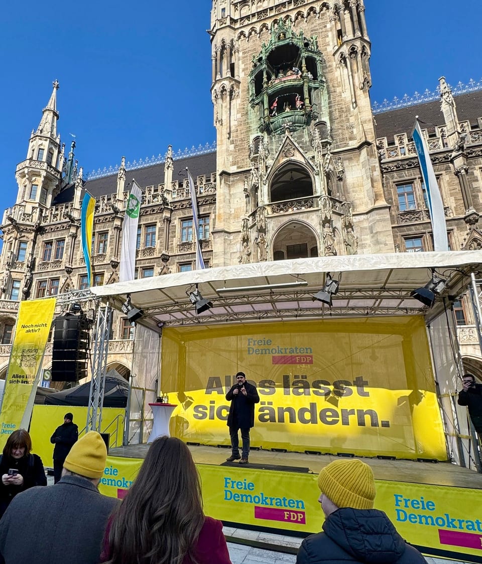 Daniel Föst begrüßt die Gäste auf der Bühne am Marienplatz vor dem Neuen Rathaus, im Vordergrund Zuhörer mit gelben Mützen