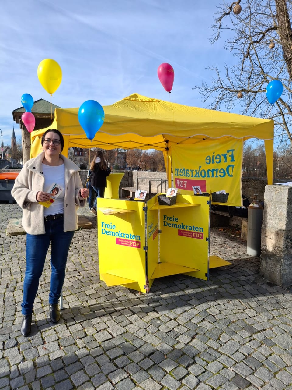 Ulla Schäfer steht mit Flyern und einem Luftballon vor dem gelben Infostand des Kreisverbands Landsberg der Freien Demokraten