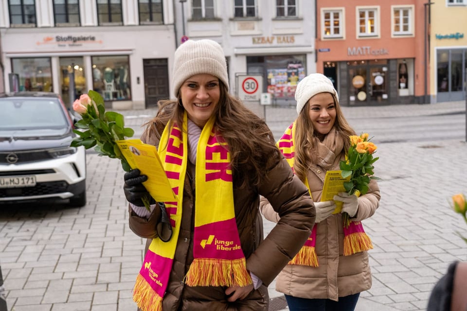 Angela Lang und Susanne Seehofer mit gelb-pinkfarbenen JuLi-Schals, Rosen und FDP-Flyern in der Landsberger Fußgängerzone