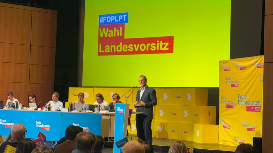 Dr. Michael Ruoff steht am Rednerpult und spricht auf der Bühne des Landesparteitags, hinter ihm eine Leinwand mit dem Schriftzug Wahl Landesvorsitz und gelbe Banner der Freien Demokraten Bayern
