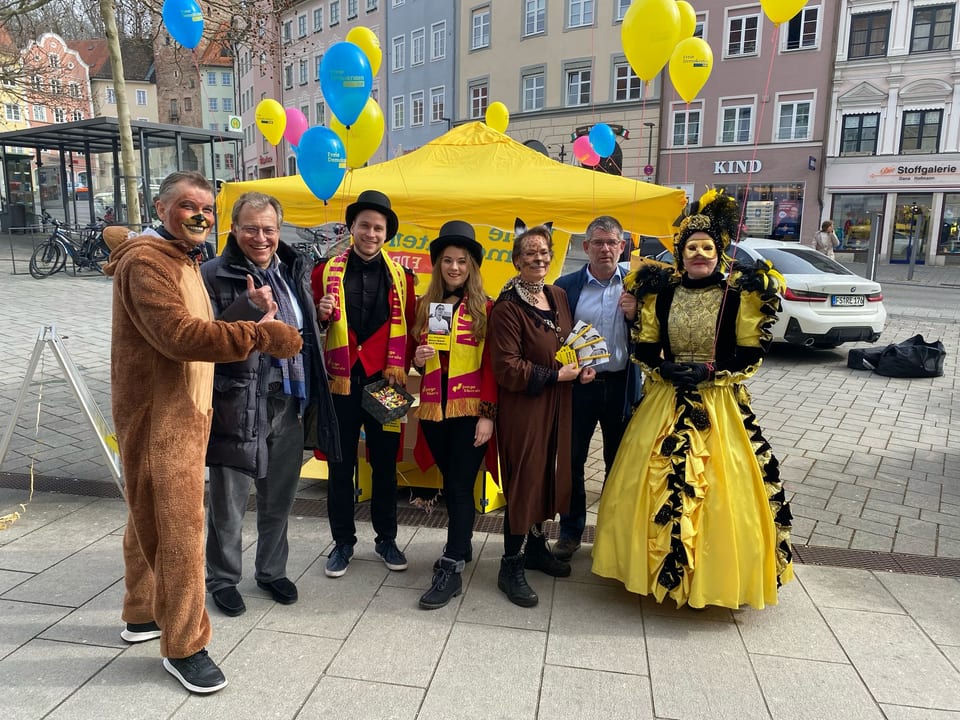 Das kostümierte Standteam des Kreisverbands vor dem gelben FDP-Pavillon: unter anderem ein Bärenkostüm, zwei Zirkusdirektoren mit Zylinder und eine Dame im goldgelben venezianischen Kostüm mit Feder-Maske, dazu gelbe und blaue Luftballons