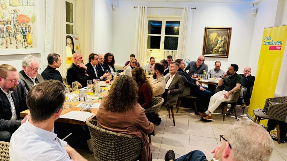 Blick in den Veranstaltungsraum mit dem sitzenden Publikum des Impulsdialogs, rechts ein gelbes FDP-Rollup