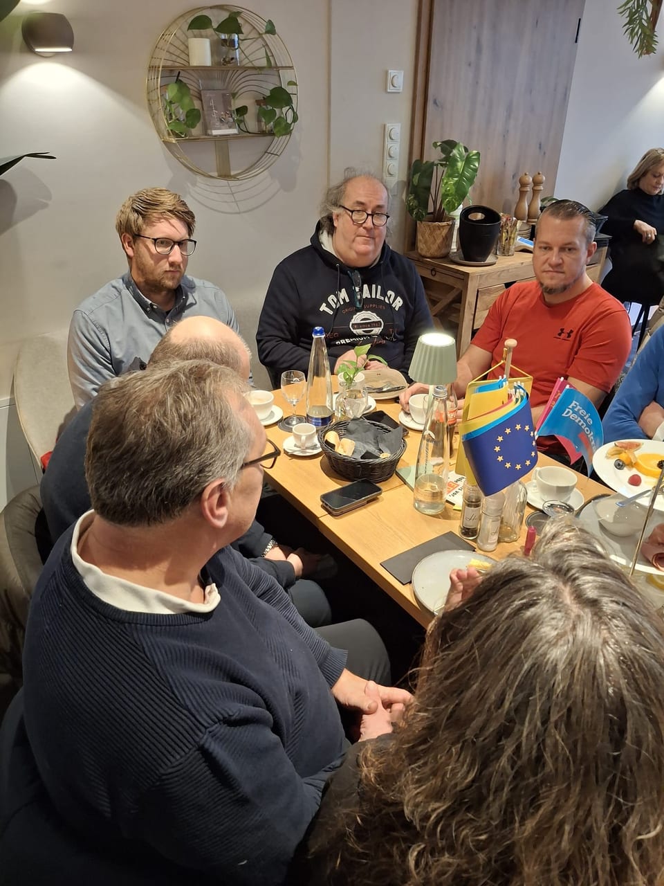 Mehrere Teilnehmer hören aufmerksam am Frühstückstisch zu, darunter Gäste aus dem Kreisverband Unterallgäu, mit FDP- und Europafähnchen auf dem Tisch