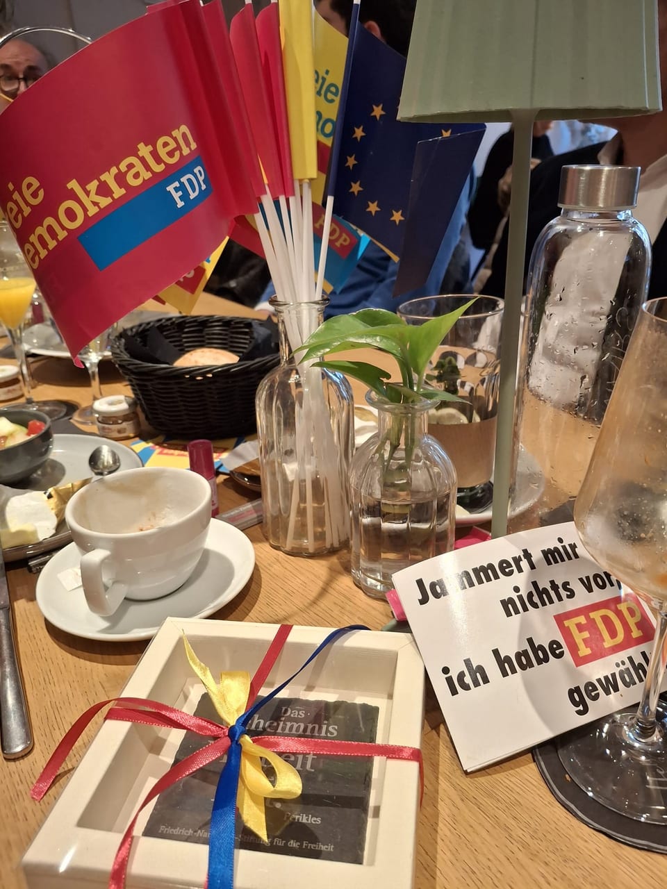 Tischdekoration mit Fähnchen der Freien Demokraten und der Europäischen Union, einem gerahmten Freiheitszitat der Friedrich-Naumann-Stiftung und einem Schild mit der Aufschrift Jammert mir nichts vor, ich habe FDP gewählt