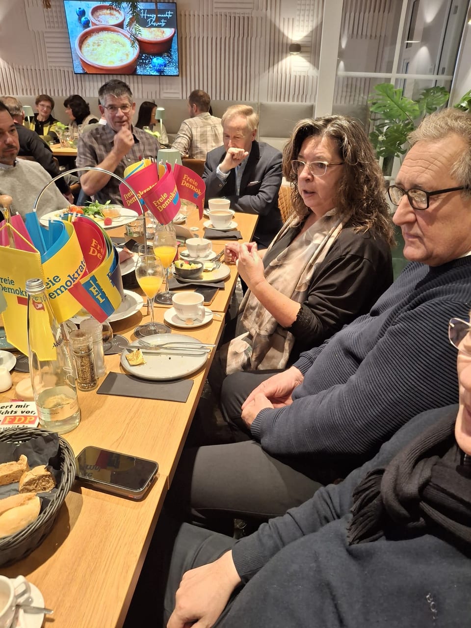 Nicole Rauscher spricht mit einer Handgeste an der langen Frühstückstafel, auf dem Tisch stehen Fähnchen der Freien Demokraten, Kaffeetassen und Gläser mit Orangensaft