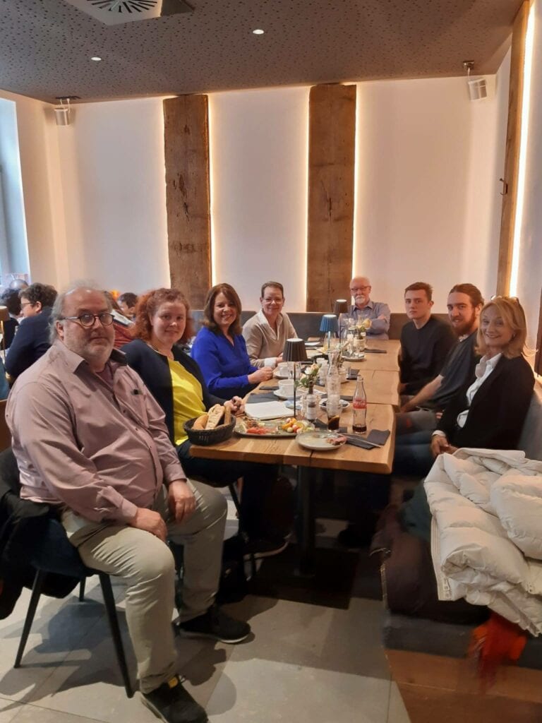 Gäste des Politischen Frühstücks an einem langen Tisch in einem hellen Café mit Holzbalken