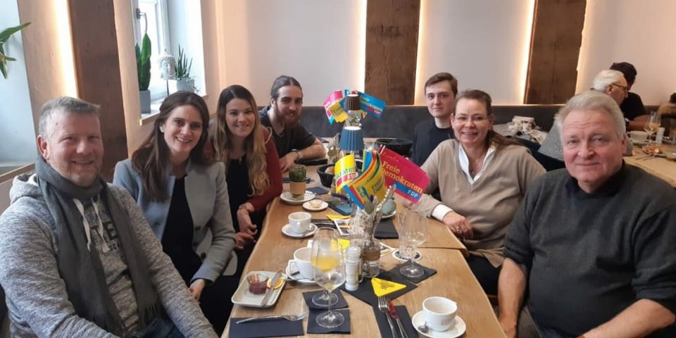 Gäste sitzen am langen Frühstückstisch mit FDP-Tischfähnchen und Kaffeetassen