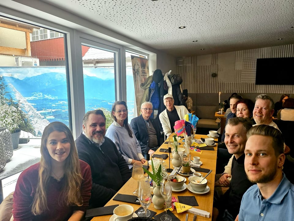 Gäste an einer langen Frühstückstafel im Café Hellmairs, auf dem Tisch FDP-Fähnchen und Flyer, im Hintergrund ein großes Wandbild einer verschneiten Berglandschaft