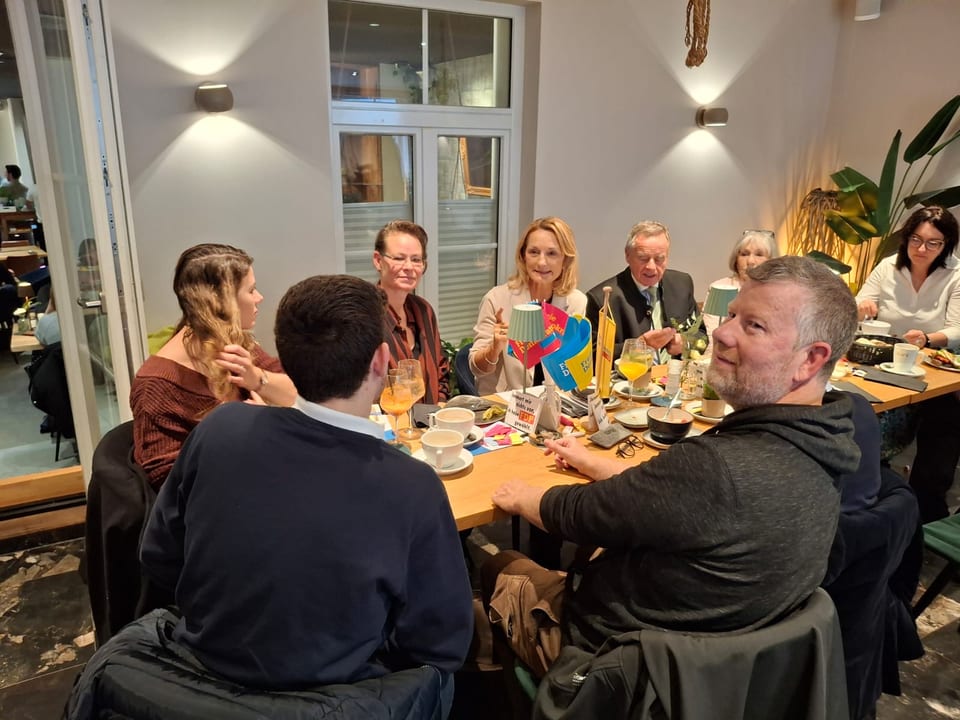 Gäste im Gespräch am Frühstückstisch im Café Hellmairs mit FDP-Tischfähnchen, Kaffee und Orangensaft