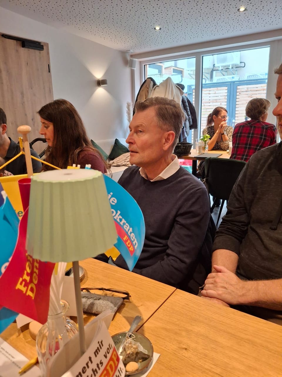Ein Gast hört aufmerksam am Frühstückstisch zu, im Vordergrund FDP-Tischfähnchen