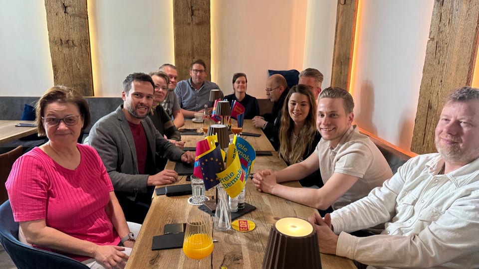Die gesamte Frühstücksrunde sitzt an einem langen Holztisch, in der Mitte FDP-Tischfähnchen und eine Europafahne, davor Gläser mit Orangensaft