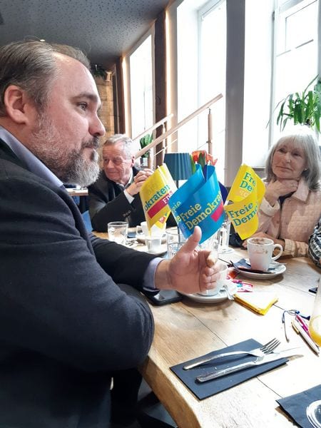 Ein Gast im Profil beim Gespräch am Frühstückstisch, davor FDP-Tischfähnchen