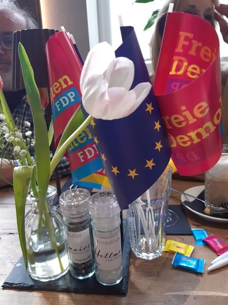 Tischdekoration mit einer weißen Tulpe, einer Europafahne und FDP-Tischfähnchen auf dem Frühstückstisch